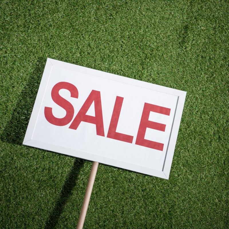 white sale banner lying on green grass, house for sale concept